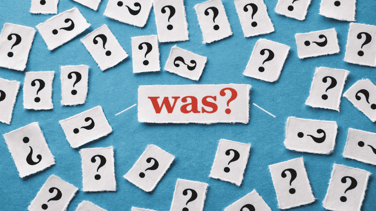 Blauer Hintergrund mit vielen Fragezeichen-Kärtchen und dem Wort „was?“ in der Mitte.