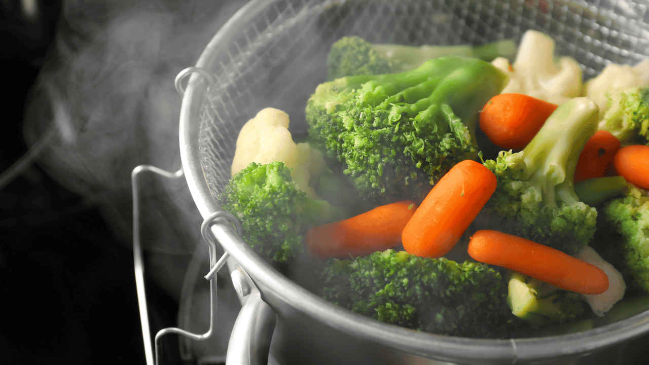 Gedünstetes Gemüse im Dampfkorb: Brokkoli, Karotten, Blumenkohl und grüne Bohnen mit sichtbarem Dampf.