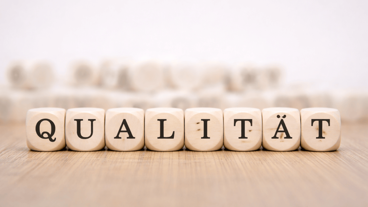 Holzwürfel mit dem Schriftzug „Qualität“ auf einem Holztisch, Hintergrund unscharf