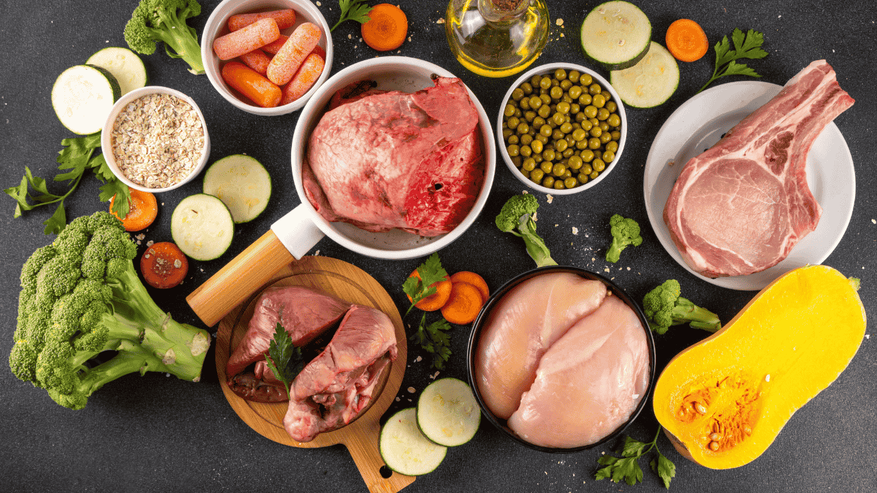 Verschiedene BARF-Zutaten für Hunde: rohes Fleisch, Innereien, Huhn, Gemüse, Haferflocken, Erbsen und Öl.