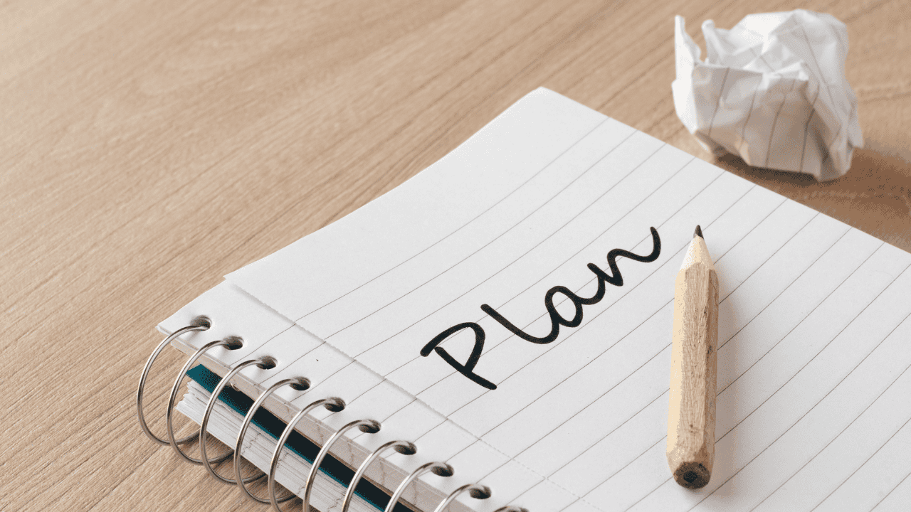 Notizblock mit dem Wort „Plan“ und Bleistift auf Holztisch.